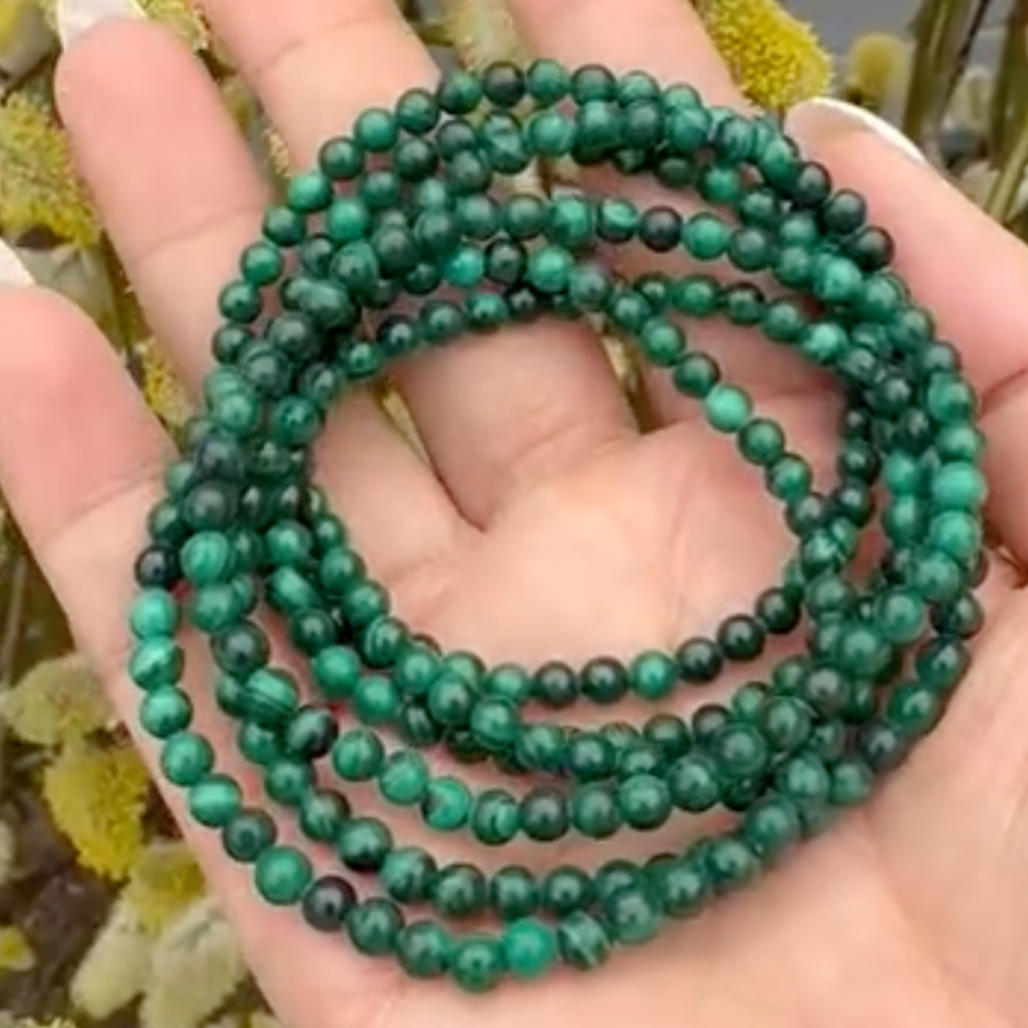 Green beaded bracelet held in a hand with a blurred natural background